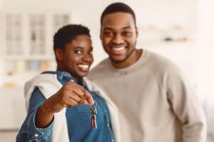 New Home. Portrait Of Happy Black Couple Showing Keys Close To Camera, Man And Woman Embracing After Moving In Own House Standing Indoor. Selective Focus, Shallow Depth, Blurred Background photo