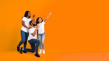 Special Offer. Cheerful African American Family Of Three People Looking Aside And Pointing Fingers Up And Aside At Free Copy Space On Yellow Background, Presenting Empty Place For Advert, Banner photo