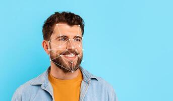 A man with a beard smiles while facial recognition technology is displayed over his face against a bright blue backdrop, showcasing modern biometric innovations. photo