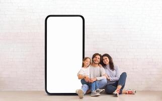 A family of three enjoys quality time together while seated on the floor, framed by a large blank screen. They are smiling and relaxed in a stylish, minimalist environment. photo