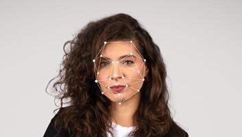 A woman stands against a plain background while facial recognition markers are displayed on her face. She has curly hair and a confident expression as the technology analyzes her features. photo