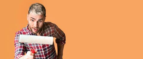 Funny millennial handsome man with paint roller isolated on yellow background photo