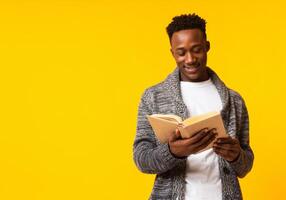 Romantic african guy reading poetry in old book on yellow background, copy space photo