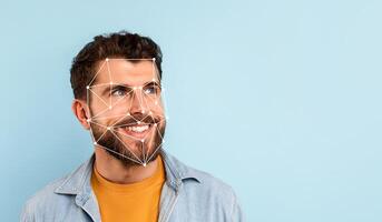 A cheerful man stands against a blue background, showcasing a facial recognition overlay that emphasizes his features. He appears friendly and engaged while looking to the side. photo