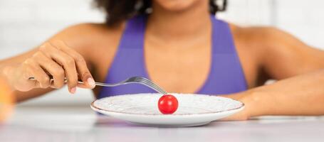 Tired About Diet. Sad african woman looking at one small tomato on a plate, holding fork, not happy at all photo
