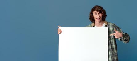 Funky millennial guy pointing at poster with empty space for your ad on turquoise background photo