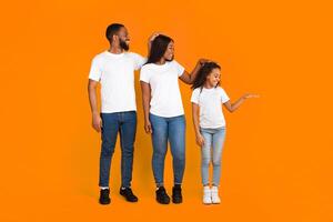 Full body length size photo of three members of family measuring height with hand palm. Smiling mum, dad and daughter cheking growing up development standing isolated on yellow orange color background