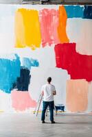 An artist stands in front of a large abstract mural with bold color blocks photo