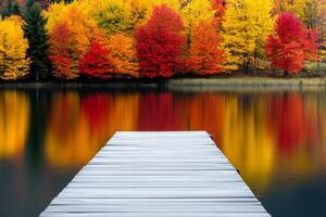 A tranquil lake scene with a wooden pier leading to water reflecting vibrant red, orange, and yellow autumn trees photo