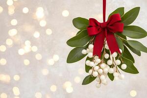 A festive sprig of Christmas mistletoe adorned with a red ribbon hanging above twinkling lights at holiday time photo