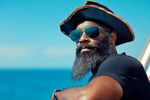 A serious pirate with a long beard and tricorn hat leans against the ship railing overlooking the blue sea and sky photo