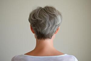 Minimalist portrait of a woman with short gray hair standing in a softly lit room against a blank wall photo