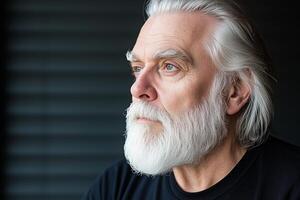 Elderly man with long white hair and beard gazes thoughtfully against a dark architectural backdrop photo