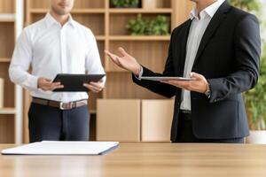 Man gestures during a discussion with a colleague holding a tablet in a modern office environment photo