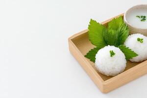Minimalist presentation of rice balls and shiso leaves on a wooden tray against a clean white background photo