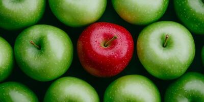 A vibrant red apple stands out among a group of green apples in a top-down view, showcasing a striking contrast photo