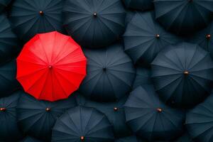 A single red umbrella stands out among numerous black umbrellas creating a striking visual contrast photo