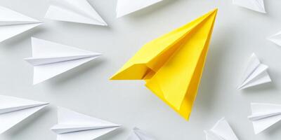 A single yellow paper airplane flies confidently in a different direction, surrounded by several white paper airplanes photo