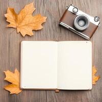 Vintage camera and travel notebook with autumn leaves on wooden table inviting exploration and adventure photo
