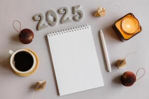 Goals 2025 concept. New Year Routine. Empty notebook, pen, cup of coffee, burning candle and paper honeycomb baubles. Flat lay style photo