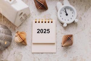 Desk calendar for 2025, alarm clock and festive decoration on the table. New Year and Christmas decoration. Planning of new year goals. Top view, flat lay photo