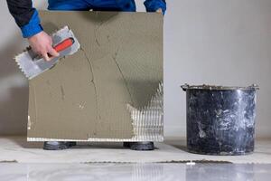 Tiler worker placing or tiling gray ceramic tile in the position over adhesive glue with lash tile leveling system, renovation or recontruction, concept of building photo