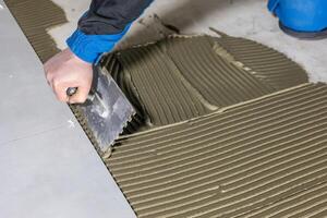 Tiler worker placing or tiling gray ceramic tile in the position over adhesive glue with lash tile leveling system, renovation or recontruction, concept of building photo
