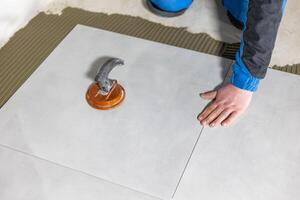 Tiler worker placing or tiling gray ceramic tile in the position over adhesive glue with lash tile leveling system, renovation or recontruction, concept of building photo