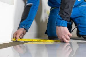 Tiler worker placing or tiling gray ceramic tile in the position over adhesive glue with lash tile leveling system, renovation or recontruction, concept of building photo