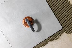 Tiler worker placing or tiling gray ceramic tile in the position over adhesive glue with lash tile leveling system, renovation or recontruction, concept of building photo