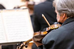 Professional symphonic string orchestra performing on stage and playing a classical music concert, violinist in a foreground photo