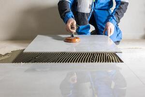 Tiler worker placing or tiling gray ceramic tile in the position over adhesive glue with lash tile leveling system, renovation or recontruction, concept of building photo