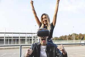 beautiful cheerful couple exulting in front of a stadium with virtual reality glasses photo