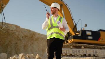 Engineer instructing worker in excavator drill machine using walkie talkie radio set at quarry video