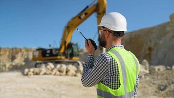 Foreman in uniform giving commands to employee in excavator using walkie talkie at construction site video