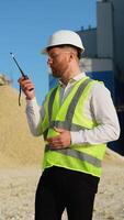 Foreman instructing workers using walkie talkie radio set at quarry. Vertical video