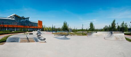 Panorama of empty public skateboard ramp park made of cement. Outdoors children's playground in skatepark for skateboarders, bmx riders and roller skates consisting of ramp, quarter, grindbox, rail photo
