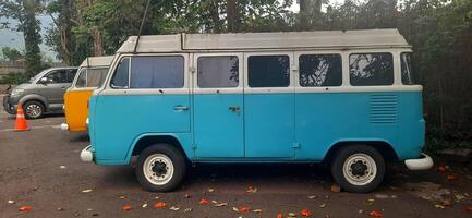 A blue and yellow minibus classic VolksWagen VW camper van parked in the street. Bandung, West Java, Indonesia - October 28 2024 photo
