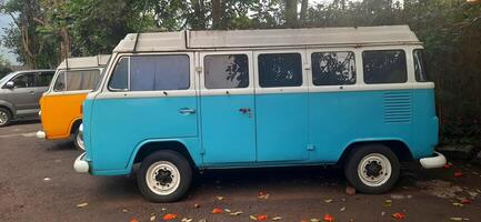 A blue and yellow minibus classic VolksWagen VW camper van parked in the street. Bandung, West Java, Indonesia - October 28 2024 photo