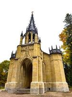 An imposing Gothic-style chapel with a tall, intricately detailed spire reaching into the overcast sky. The structure stands with its arched entrance and stone facade, embodying historical photo