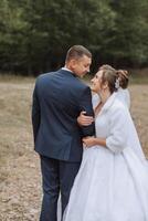 A bride and groom are standing in a field, smiling at the camera photo