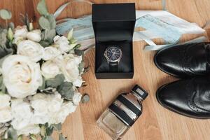 A black box with a watch inside sits on a wooden table next to a bouquet of whit photo