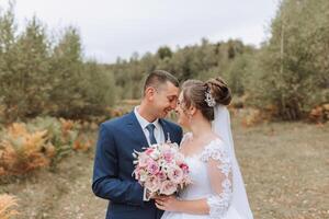 A bride and groom are standing in a field, smiling at the camera photo