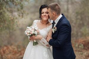 A bride and groom are hugging each other in a forest photo