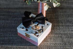 A box with a bow on top of it and two rings inside photo