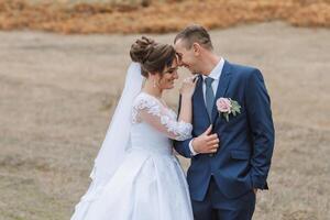 A bride and groom are standing in a field, smiling at the camera photo