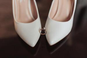 A pair of white shoes with a diamond ring on the left shoe photo