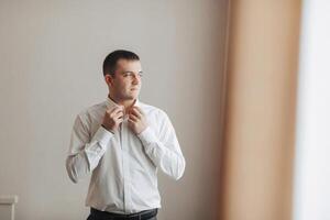 A man in a white shirt is getting dressed in front of a window photo