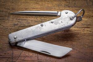 vintage sailor knife with marlinespike and straight blade, made in Poland in 1970s, against rustic wood, signs of heavy use and abuse photo