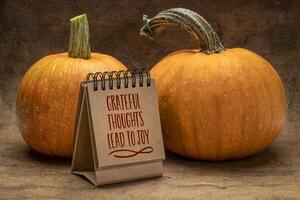Grateful thoughts lead to joy - handwriting in a desktop calendar with pumpkins, November and Thanksgiving season concept photo